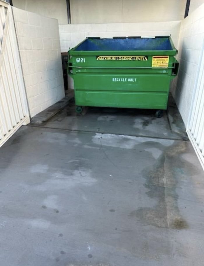 Dumpster enclosure interior washed out β slab and walls recovered around the recycle bin