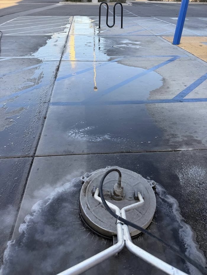 Hot-water surface cleaner lifting years of grime from a retail sidewalk β the cleaned path against the untouched concrete